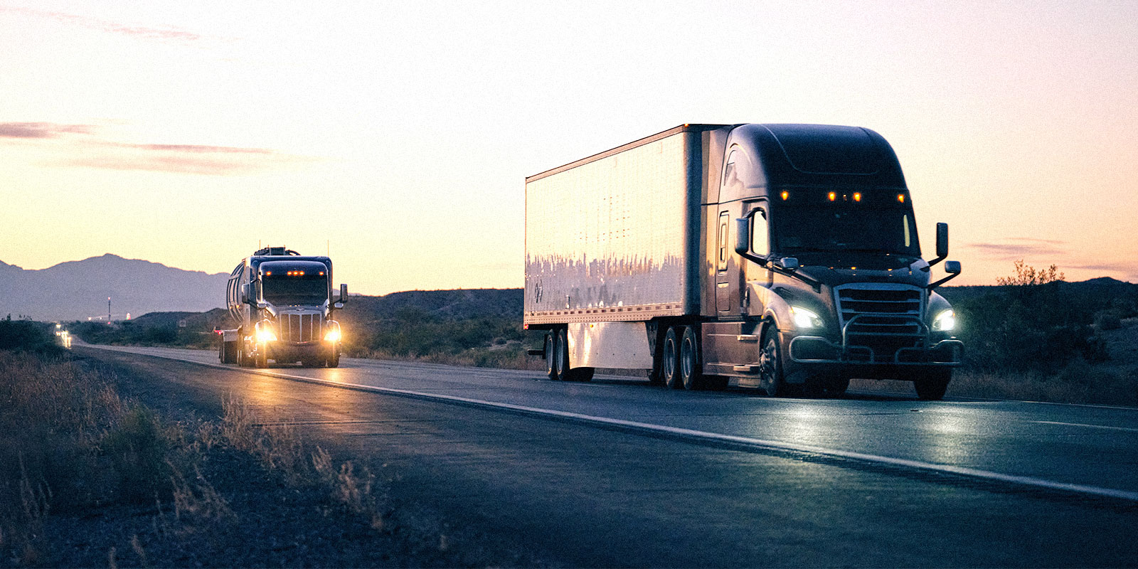 Two freight trucks driving at sunset